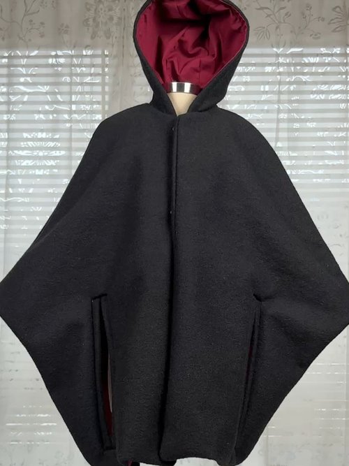 Vordere Ansicht eines schwarzen Capes mit rotem Futter und Kapuze