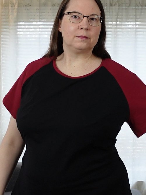 Frau in schwarzem T-Shirt mit roten Raglan-Ärmeln, ein Arm ausgestreckt