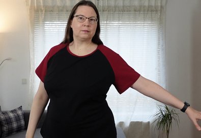 Frau in schwarzem T-Shirt mit roten Raglan-Ärmeln, ein Arm ausgestreckt